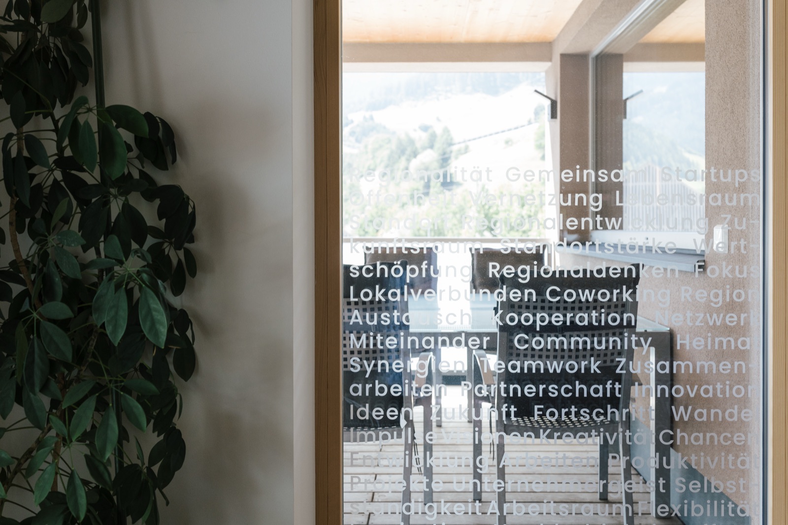 Blick von der Ideenkuchl auf die Terrasse mit Sitzgelegenheiten und beschrifteter Glastür